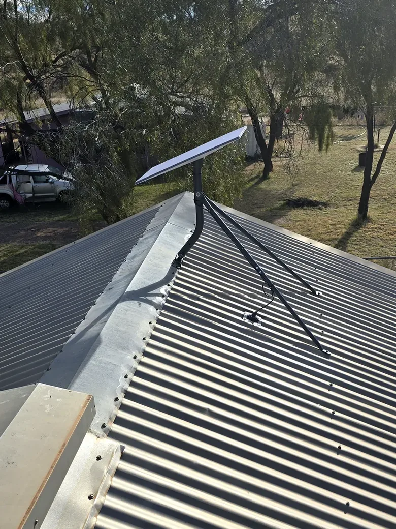 Starlink dish pole-mounted on a corrugated roof ridge with stay wires and a neat cable run, installed near Alice Springs